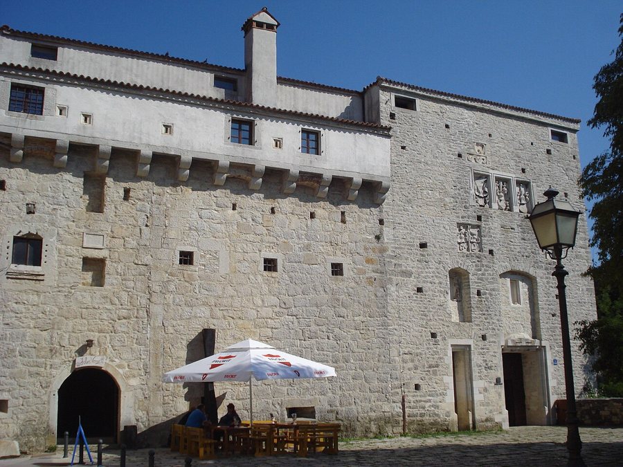 Die helle steinerne Westfassade der Burg Pazin mit vorspringenden Wehrerkern über dem Eingang.